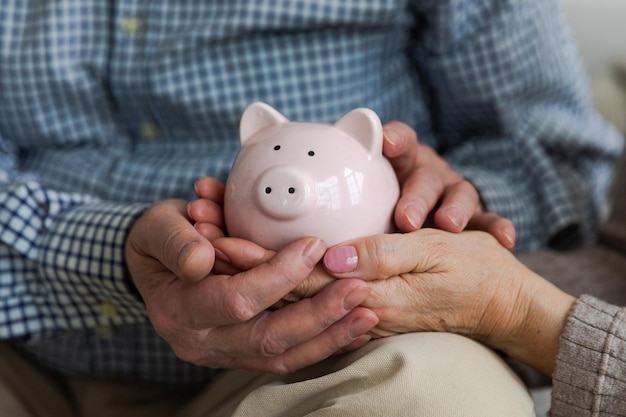 Oszczędzanie pieniędzy na inwestycję dla przyszłej starszej dorosłej pary dojrzałych rąk trzymając skarbonkę z pieniędzmi