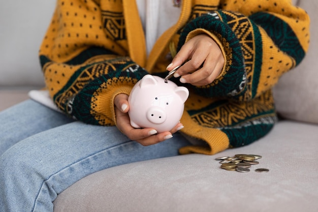 Oszczędzanie pieniędzy na inwestycję dla przyszłych kobiecych rąk trzymających różową skarbonkę i wkładających monety