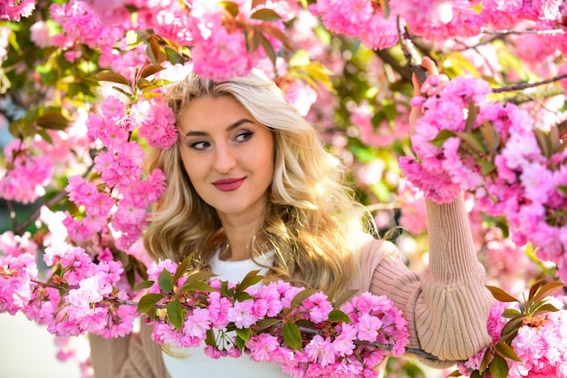 Otaczające ją różowe kwiaty Wiosenna natura Urocza kobieta makijaż twarz blond włosy Nurkowanie w rozkwicie sakury Kwiaty sakury Ekstrakt z kwiatów Olejki eteryczne Kosmetyki naturalne Perfumy dla kobiet
