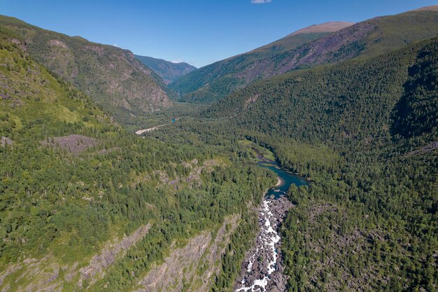 Otoczenie leśne sfotografowane z drona z widokiem na wysokie skaliste wzgórza z mnóstwem drzew i szybko płynącym wodospadem.