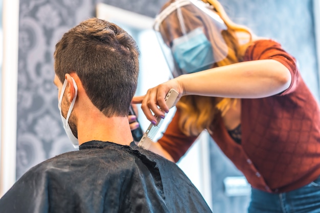 Otwarcie salonów fryzjerskich po pandemii koronawirusa, Covid-19. Środki bezpieczeństwa, maska na twarz, ekran ochronny, dystans społeczny. Blonde Caucasian Hairdresser Working