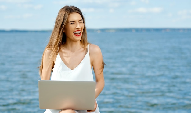 Otwarcie śmiejąca się kobieta z laptopem rozbiera się na bok przed jeziorem. Zdjęcie wysokiej jakości