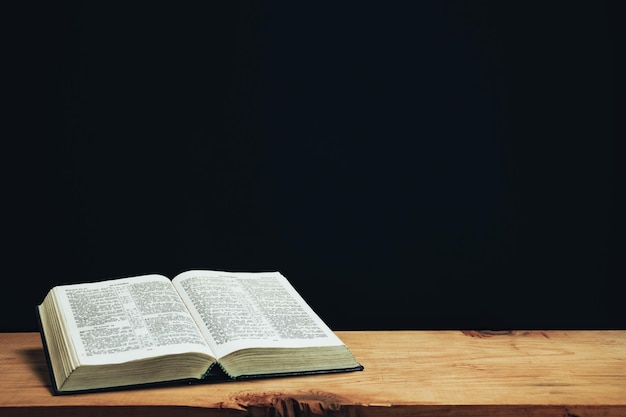 Otwarta Biblia na czerwonym starym drewnianym stole Piękne czarne tło na ścianie