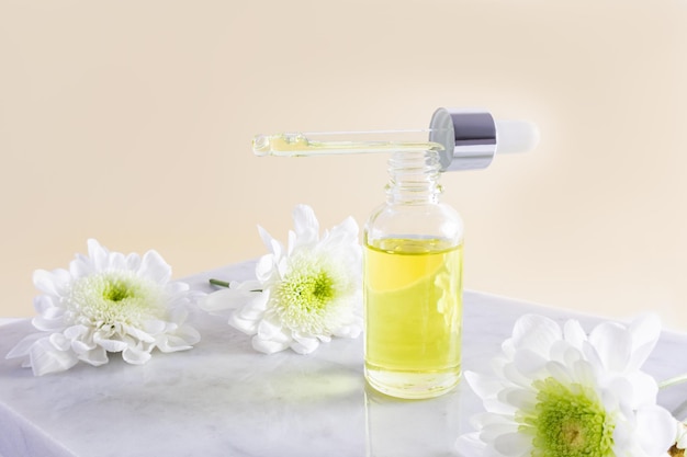 Otwarta butelka kosmetyczna wypełniona pipetą naturalnego oleju organicznego lub serum do pielęgnacji twarzy i ciała beżowym marmurowym podium
