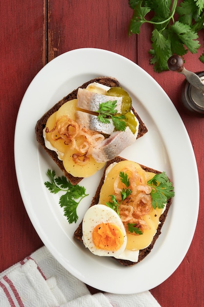 Otwarta kanapka lub smorrebrod z chlebem żytnym śledzia jajka karmelizowane cebula pietruszka i ser na starym drewnianym, wiejskim tle stołu duńskie lub skandynawskie tradycyjne jedzenie przekąski obiad