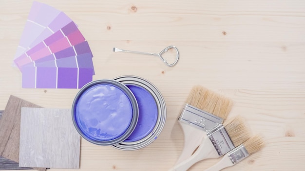 Otwarta metalowa puszka po farbie z fioletową farbą i innymi narzędziami malarskimi na niedokończonym drewnianym tle.