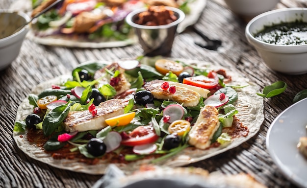 Otwarta wegetariańska tortilla z sałatką, rzodkiewką, pomidorkami cherry, oliwkami, granatem i grillowanym serem haloumi.