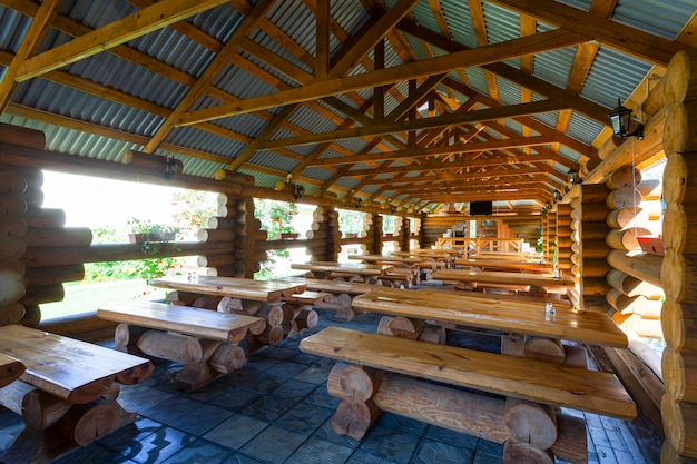 Otwarty drewniany ganek z dużą ilością drewnianych stołów z ławkami.