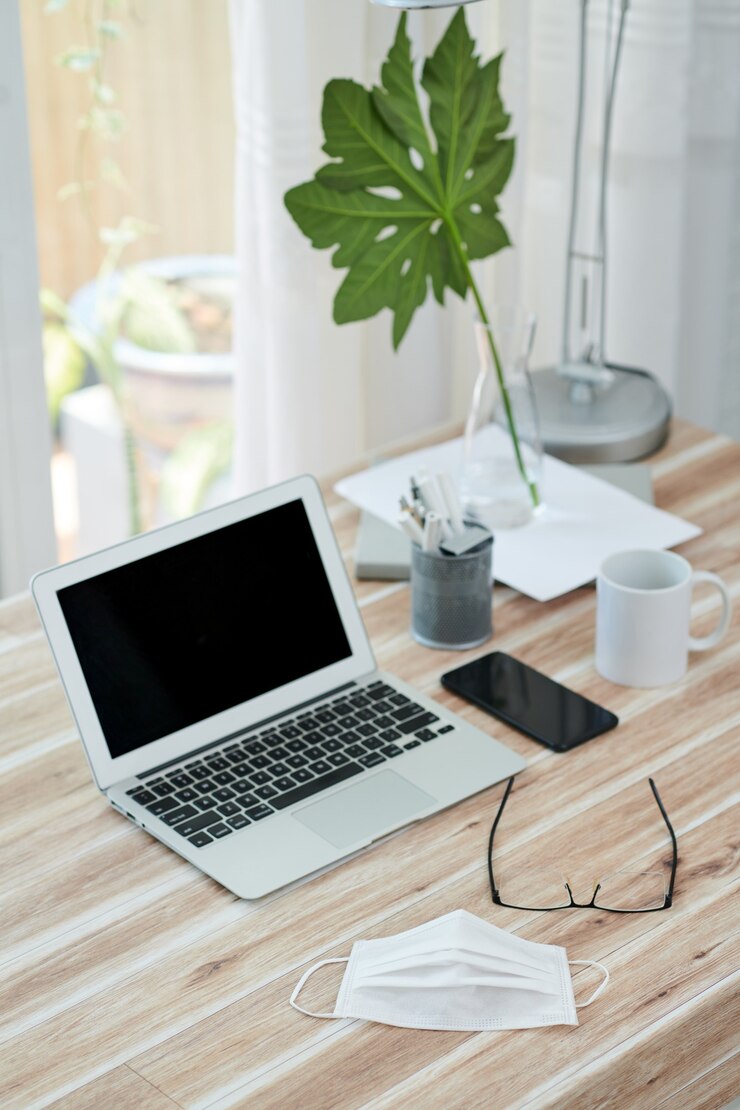 Zdjęcie otwarty laptop, okulary i maska medyczna na biurku osoby biznesowej lub studenta