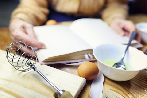 Zdjęcie otwórz książkę kucharską w rękach starszej kobiety przed stołem z naczyniami