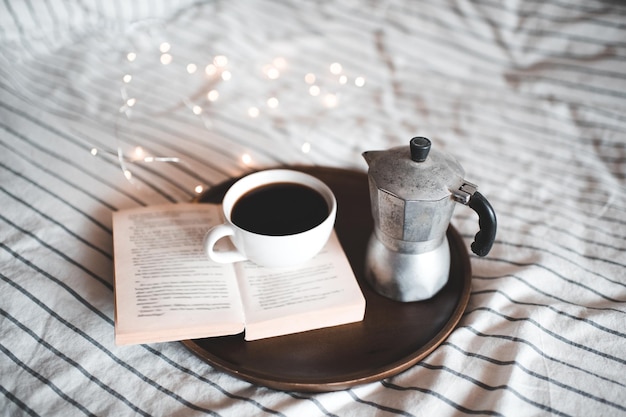 Otwórz książkę z filiżanką kawy i ekspresem do kawy w łóżku zbliżenie. Dzień dobry. Śniadanie.