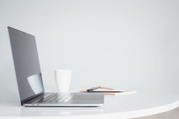 Otwórz laptopa z kawą i notatnikiem na białym stole