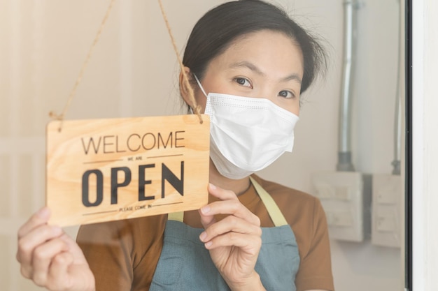 Zdjęcie otwórz ponownie azjatycki młody właściciel detaliczny sklep z kawą kobieta obracając tablicę otwórz nosząc maskę na twarz chroń przed pandemią koronawirusa ponownie otwórz sklep po zamknięciu kwarantanna w covid19 nowa normalna