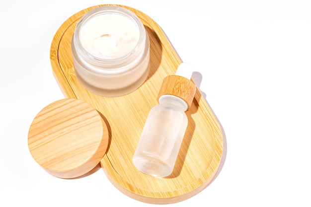 Zdjęcie otwórz słoik kremowy i butelkę kroplówkową z olejem do twarzy na bambusowej tacce makiety pojemników kosmetycznych tło dla prezentacji marki i opakowania koncepcja produktu kosmetycznego do pielęgnacji skóry naturalnej
