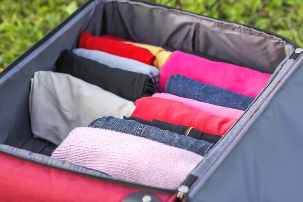 Otwórz walizkę na zielonej trawie z różnymi ubraniami złożonymi pionowo. Pionowe przechowywanie dla łatwego pakowania w podróży.