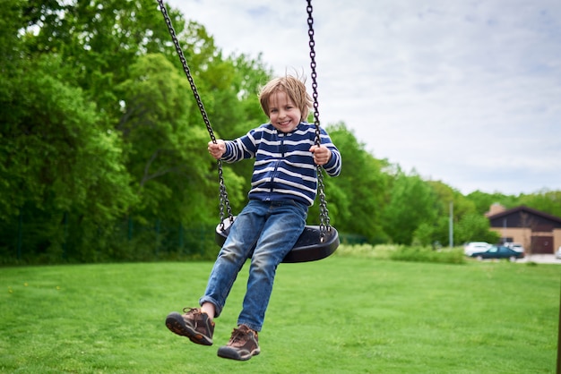 Outdoors portret ślicznego preschool roześmiany chłopiec huśta się na huśtawce przy boiskiem