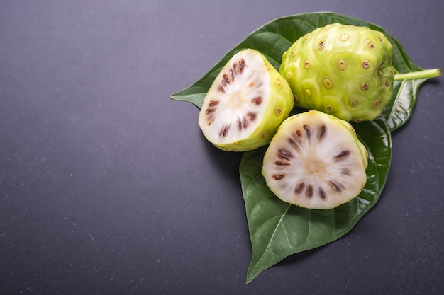 Owoc Wielkiego morinda (Noni) lub Morinda citrifolia drzewo i zielony liść na czarnym kamieniu