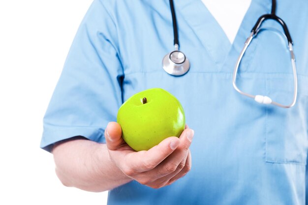 Owoce sprawiają, że jesteś zdrowy. Zbliżenie chirurga w niebieskim mundurze trzymającego zielone jabłko stojąc na białym tle