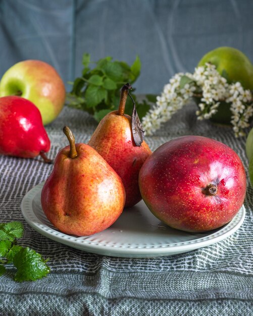 Owoce umieszczone na zielonym obrusie jabłka gruszki i mango z gałązkami mięty na zielonej płaskiej płytce