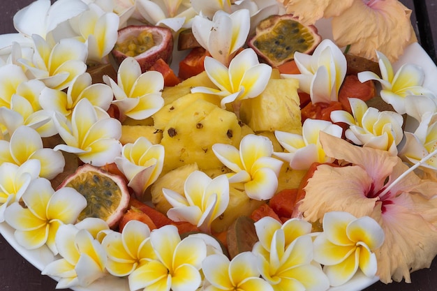 Owocowa sałatka deserowa z ananasową papają, marakują i białym kwiatem frangipani na talerzu