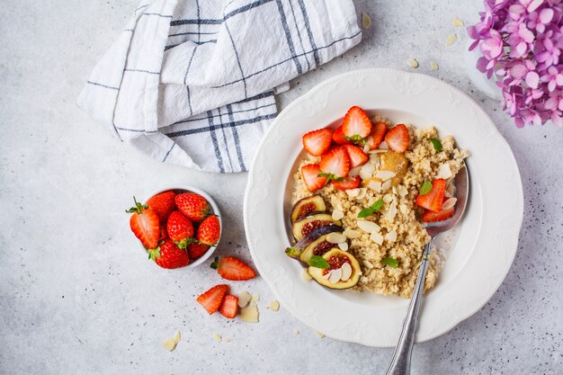 Owsianka Quinoa z truskawkami i figami w białej płytce. Zdrowe śniadanie.