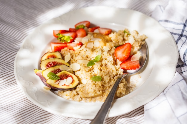 Owsianka Quinoa z truskawkami i figami w białej płytce. Zdrowe śniadanie.