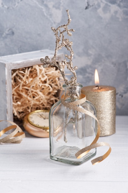 Ozdobna butelka ze złotymi gałązkami, zapalona świeca i świąteczna wstążka ze złotym dekorem.