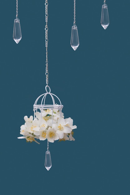 Ozdobna klatka z kwiatami jaśminu i szklanymi zawieszkami na łańcuszkach na turkusowym tle Piękna świąteczna koncepcja ślubu