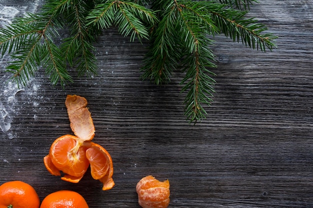 Ozdoby świąteczne i noworoczne w postaci mandarynek i zielonej choinki na drewnianej powierzchni posypanej białym śniegiem