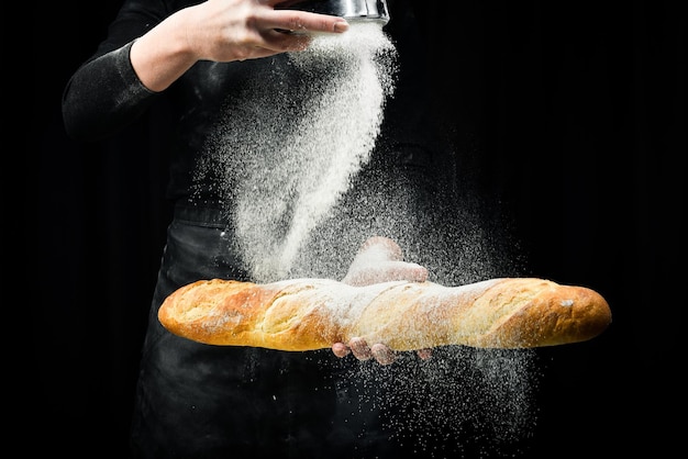 Pachnąca świeża bagietka w dłoniach. Czarne tło do gotowania. Na białym tle na czarnym tle.