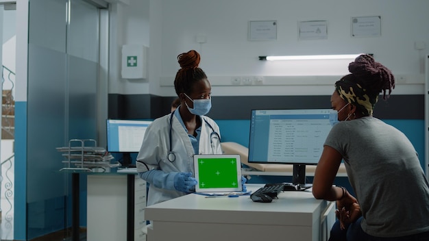 Pacjent i medyk patrzący na poziomy zielony ekran na tablecie i noszący maski na twarz dla ochrony. Kobieta i lekarz robią sprawdzanie z kluczem chroma i szablonem makiety na białym tle.