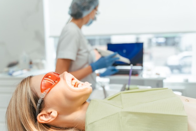 Pacjent Siedzący Na Krześle Dentystycznym Z Otwartymi Ustami W Czerwonych Okularach Do Wybielania I Leczenia Zębów