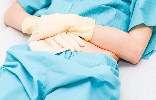 Pacjent w piżamie z otwartym brzuchem naciska worek kolostomiczny rękami w sterylnych rękawiczkach