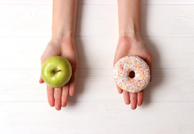 Pączek i jabłko w kobiecych rękach zdrowy i niezdrowy wybór żywności