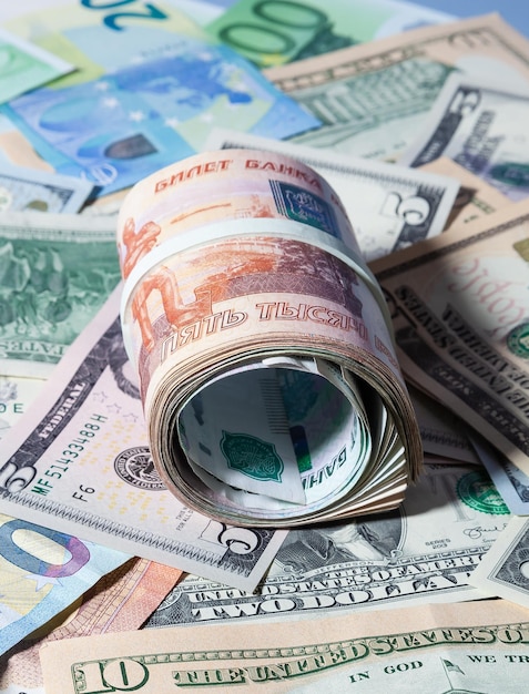Paczka rosyjskich papierowych pieniędzy w nominałach 1 i 5 tys. rubli zwinięta leży nad amerykańskimi i europejskimi papierowymi pieniędzmi USD, EUR i GBP