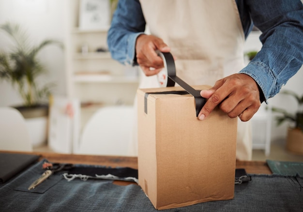 Pakowanie paczki lub zamówienia dostawy za pomocą czarnej taśmy podczas pakowania w pudełko i owijania produktu Zbliżenie właściciela małej firmy lub krawca pakującego pudełko w celu wysyłki lub sprzedaży kurierskiej