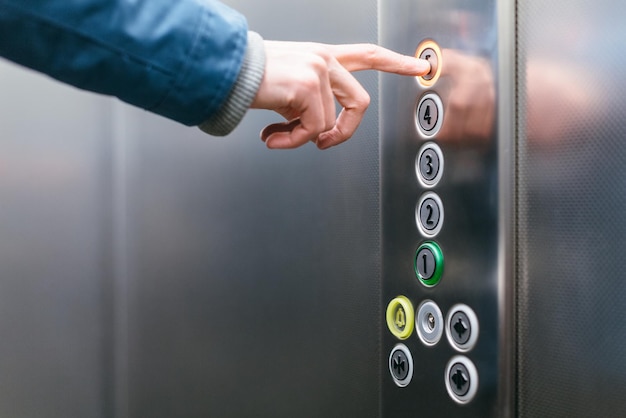 Zdjęcie palec wskazujący dorosłego mężczyzny naciskający przycisk piątego piętra w windzie windy z bliska