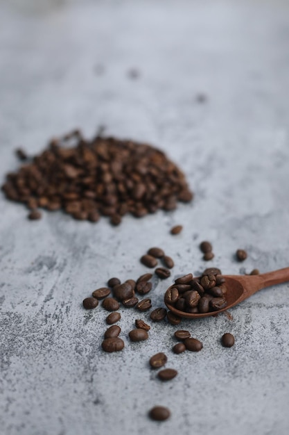 Palone ziarna kawy na drewnianej łyżce z rozmytym obrazem stosy nasion kawy na szarym tle