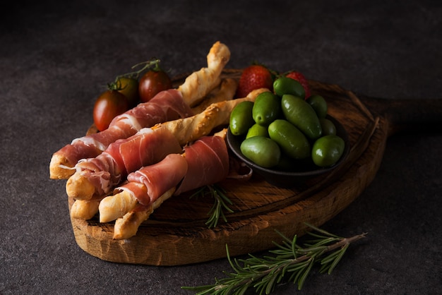 Paluszki (grissini) z prosciutto, oliwkami i pomidorami - tradycyjne włoskie przekąski do wina, selektywne skupienie