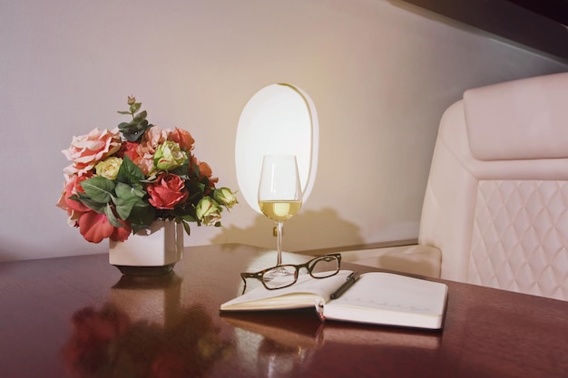 Pamiętnik z kwiatami szklane wino na stole roboczym luksusowego wnętrza w prywatnym odrzutowcu