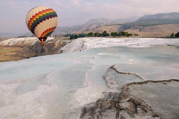 Pamukkale, Denizli, Turcja: balon na ogrzane powietrze przelatujący nad basenami trawertynowymi wapiennymi tarasami w piękny dzień