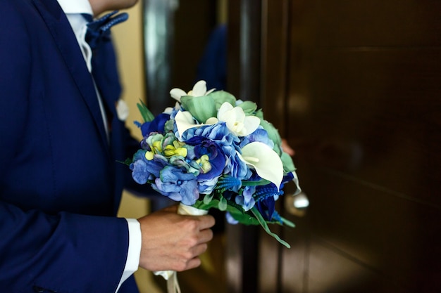 Pan młody stoi z niebieskim Bukiet ślubny przed drzwiami
