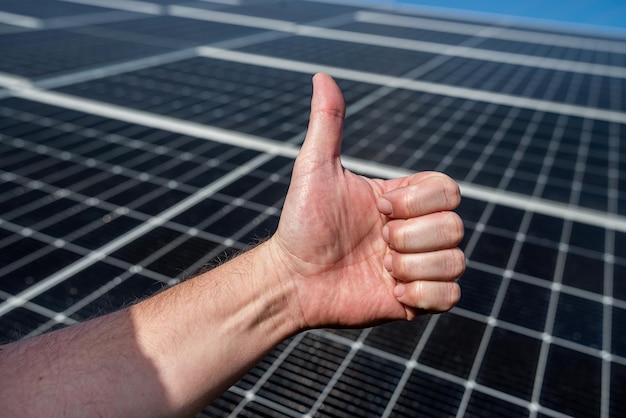Panel słoneczny na dachu wytwarza energię elektryczną na tle dłoni z palcem w górę inwestycji w oszczędzanie energii elektrycznej