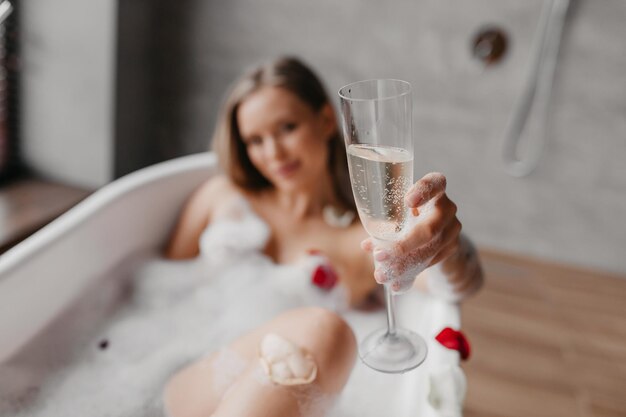 Pani odpoczywająca w spienionej kąpieli i trzymająca kieliszek szampana skupia się na dłoni z zbliżeniem napoju