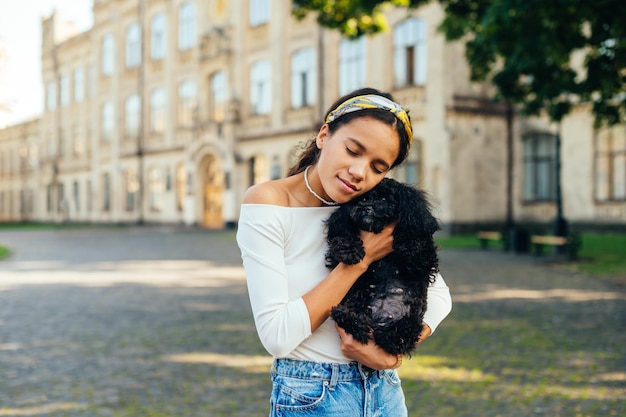 Pani stoi na ulicy na tle pięknego letniego wyglądu i przytula uroczego pieska