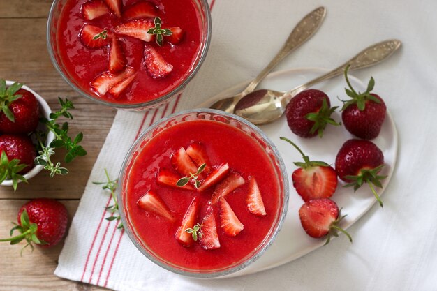 Panna cotta z sosem truskawkowym i plasterkami truskawek, ozdobiona liśćmi tymianku. Styl rustykalny.