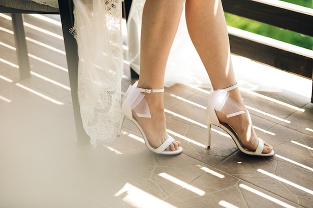 Panna młoda siedzi na sobie suknię ślubną i buty na obcasie