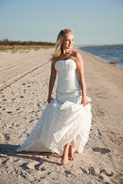 Panna młoda spaceru wzdłuż wybrzeża morskiego w pięknej sukni ślubnej.