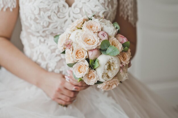 Panna młoda trzyma w dłoniach delikatny bukiet ślubny z białych piwonii i róż 2675