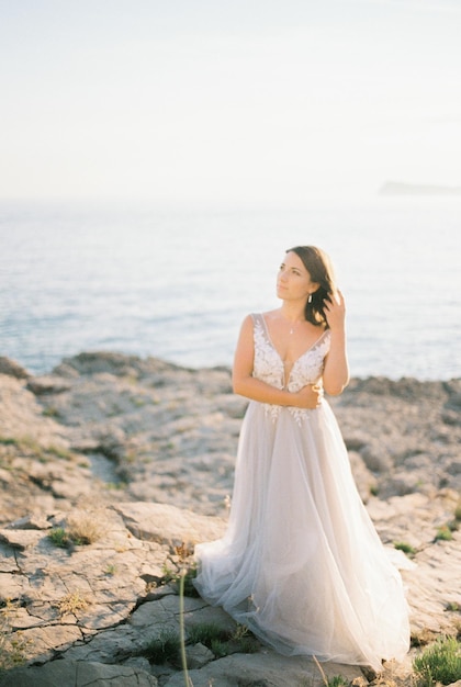 Panna młoda w białej bufiastej sukience stoi na skalistym brzegu morza